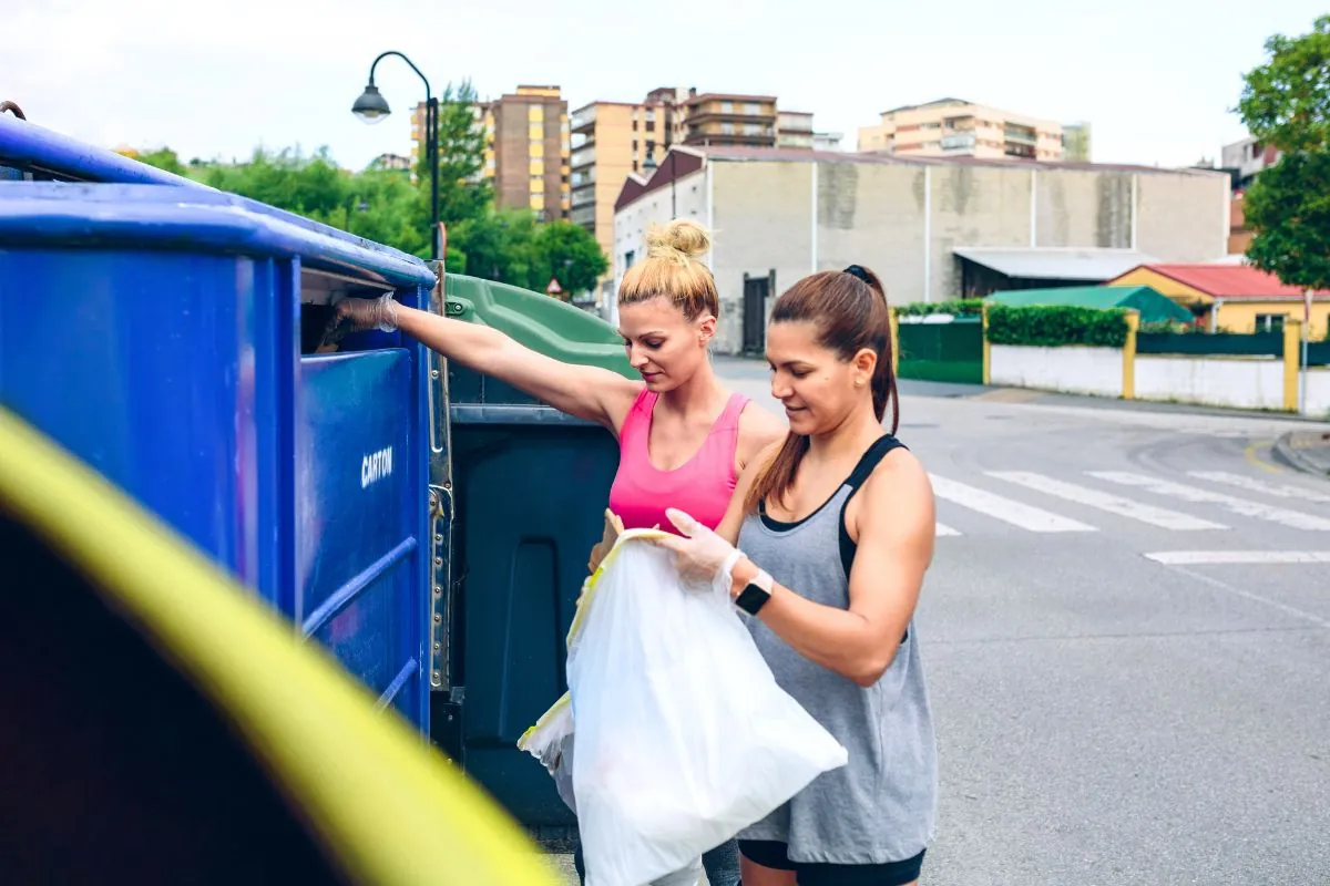 girls throwing garbage to recycling dumpster